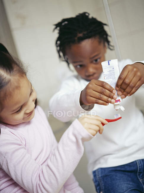 Preschooler girl and boy putting toothpaste on toothbrush. — Stock Photo