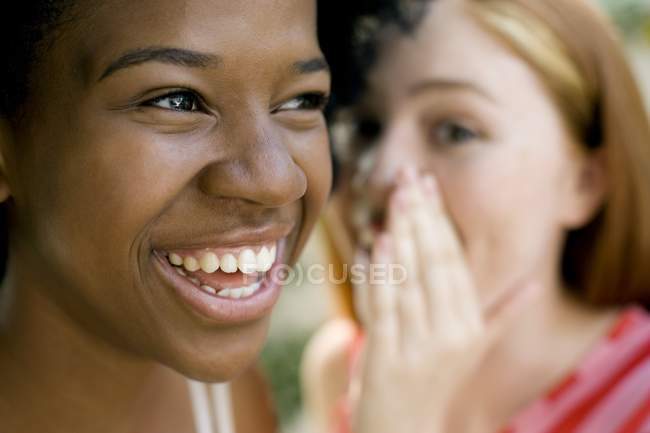 Adolescente gingembre fille chuchotant avec femme afro-caribéenne ami . — Photo de stock