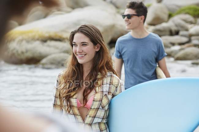 Frau am Strand mit Surfbrett und Mann im Hintergrund. — Stockfoto