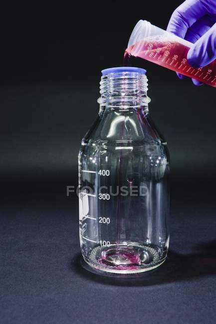Primer plano de la mano científica verter reactivo en botella para la investigación química
. - foto de stock