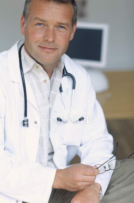 Retrato del médico del hospital sosteniendo gafas y mirando en cámara . - foto de stock