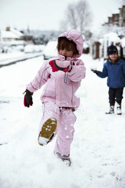 Frères et soeurs d'âge élémentaire se battant en boule de neige dans la rue . — Photo de stock