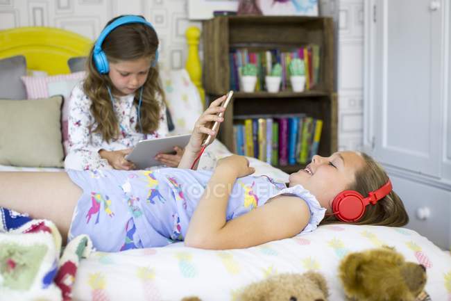 Zwei Schwestern im Schlafzimmer hören Musik und verwenden ein digitales Tablet. — Stockfoto