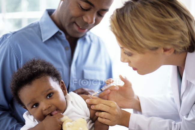 Ärztin spritzt Baby, das auf dem Schoß des Vaters sitzt. — Stockfoto