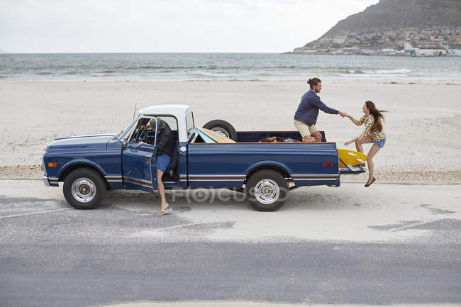 Woman getting on pick up truck with friends on beach. — Stock Photo