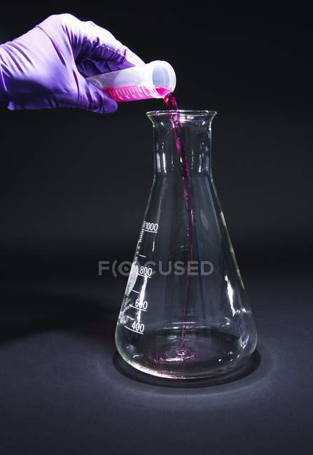 Primer plano de la mano científica vertiendo reactivo en el matraz para la investigación química
. - foto de stock