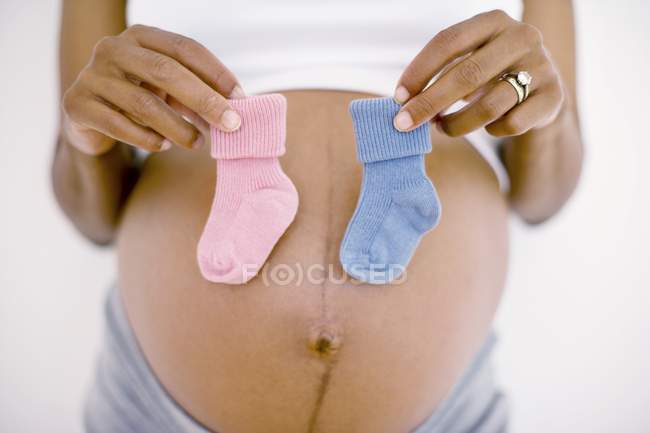 Vista recortada de la mujer embarazada sosteniendo calcetines de bebé azules y rosados - foto de stock