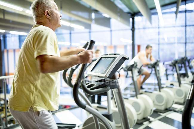Homme âgé utilisant une machine d'exercice dans la salle de gym . — Photo de stock