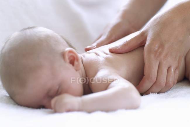 Las manos femeninas masajeando la espalda del bebé recién nacido . - foto de stock