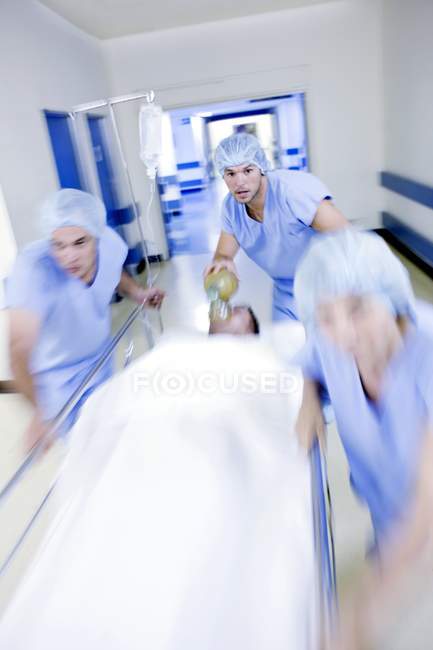 Squadra di emergenza spingendo barella ospedaliera con paziente in corridoio . — Foto stock