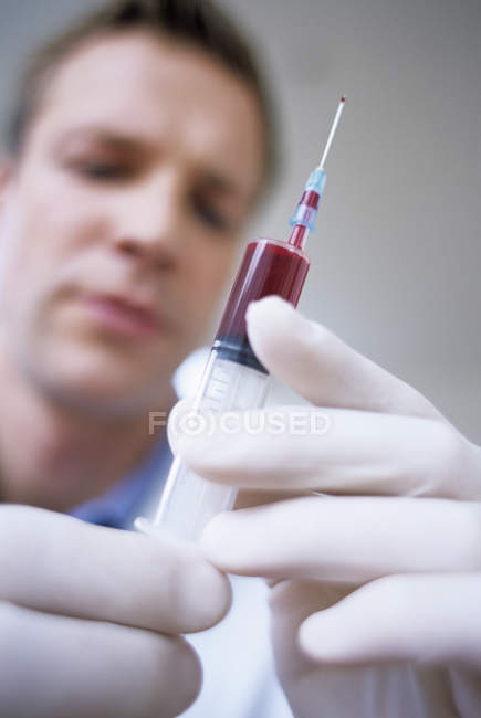 Close-up da seringa cheia de sangue nas mãos do médico masculino . — Fotografia de Stock