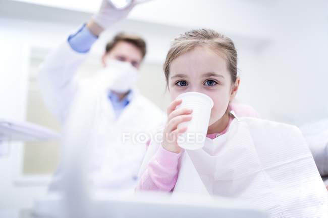 Retrato de niña bebiendo agua en clínica dental . - foto de stock