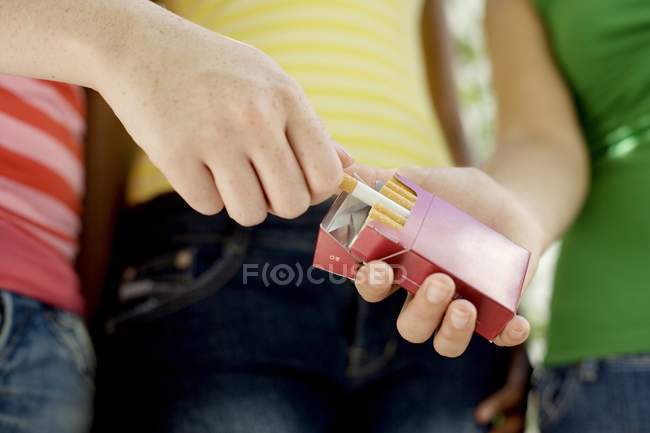 Teenage girl taking cigarette from friends packet. — Stock Photo