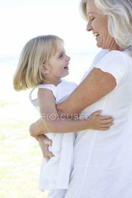 Grand-mère en vêtements blancs embrassant petite-fille sur blanc . — Photo de stock