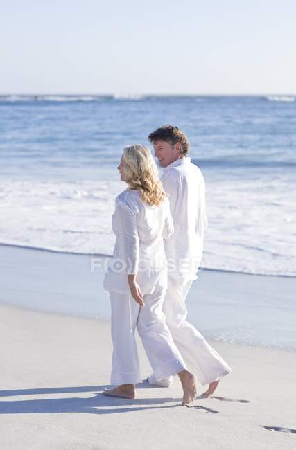 Ältere Paare gehen Arm in Arm am Sandstrand. — Stockfoto