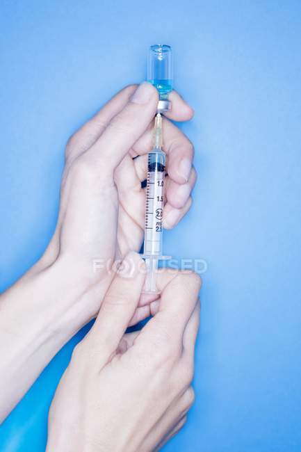Female hands filling syringe on blue background. — Stock Photo