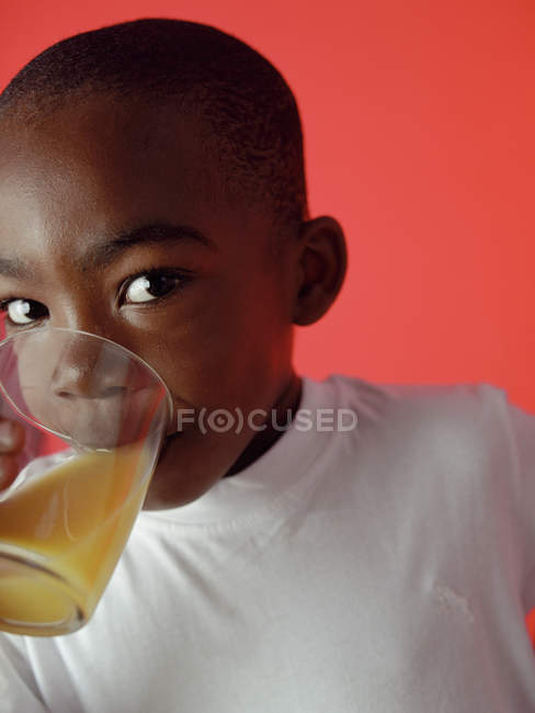 Menino beber copo de suco de laranja no fundo vermelho . — Fotografia de Stock