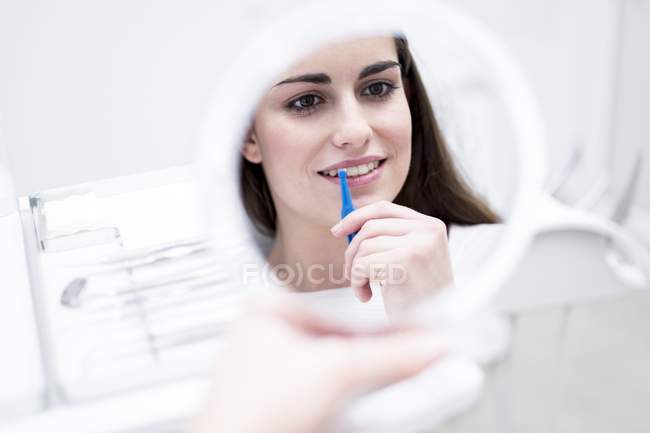 Giovane donna con spazzola interdentale e guardando nello specchio in ospedale
. — Foto stock