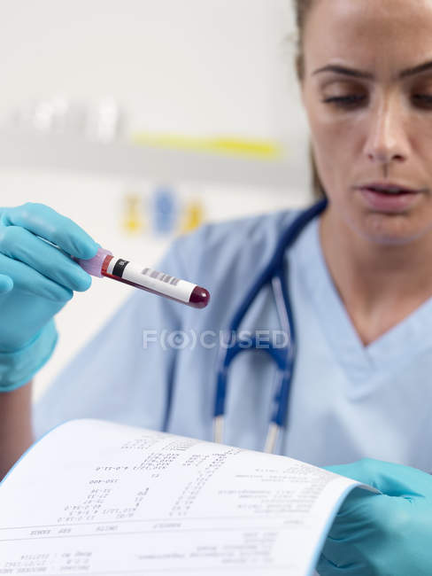 Medico che legge i risultati degli esami del sangue mentre tiene il campione di sangue
. — Foto stock