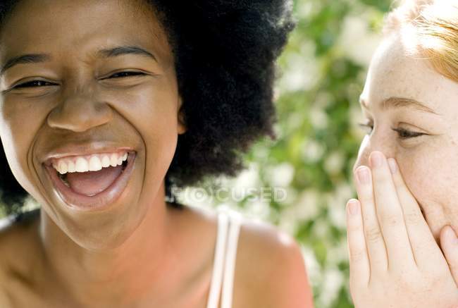 Adolescente gengibre menina sussurrando com feminino afro-caribenho amigo . — Fotografia de Stock