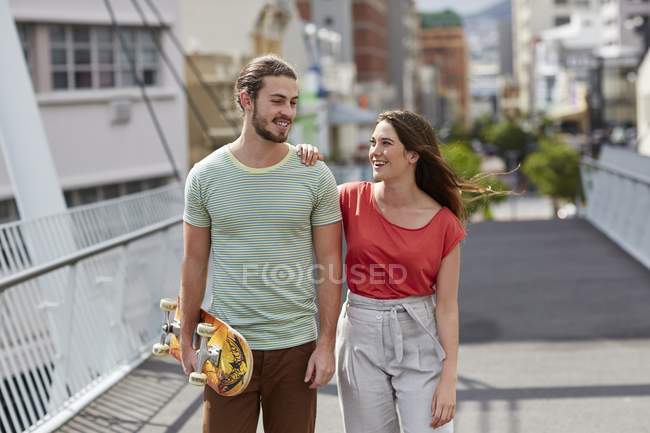 Jovem casal andando na rua e carregando skate . — Fotografia de Stock