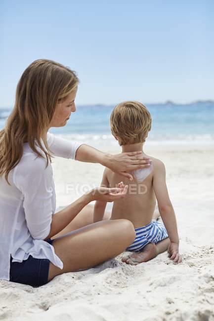 Mère appliquant de la crème solaire à son fils sur la plage . — Photo de stock
