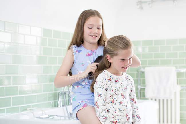 Девушка расчесывает волосы сестры в ванной комнате . — стоковое фото