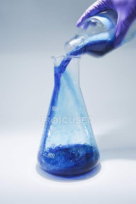 Close-up of scientist hand pouring reagent into flask for chemical research. — Stock Photo