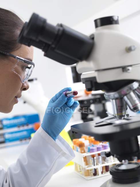 Female scientist holding blood sample by microscope in laboratory. — Stock Photo