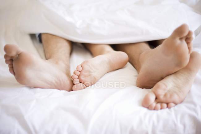 Un par de pies asomándose desde debajo del edredón en la cama . - foto de stock