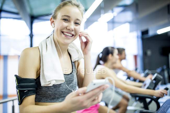 Mujer ajustando auriculares y escuchando música mientras hace ejercicio en el gimnasio
. - foto de stock