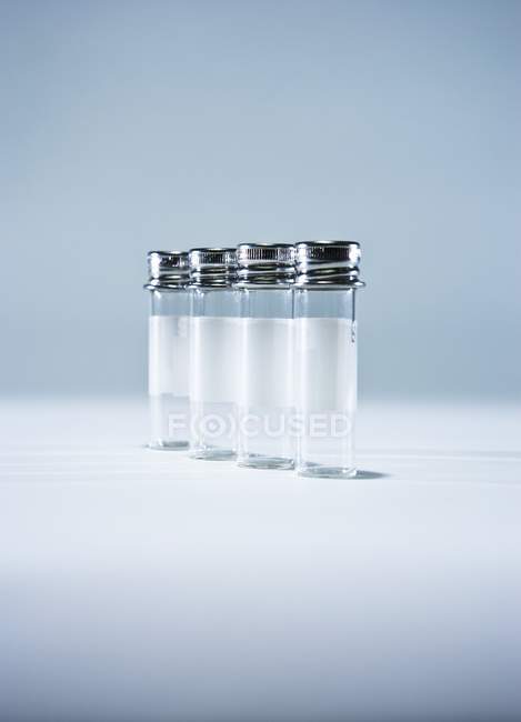 Bottiglie campione vuote con coperchi metallici in fila sul tavolo . — Foto stock