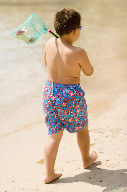 Niño caminando por la playa y sosteniendo la red de pesca . - foto de stock