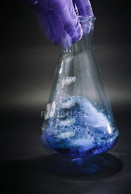 Close-up of scientist hand agitating liquid in flask for chemical research. — Stock Photo