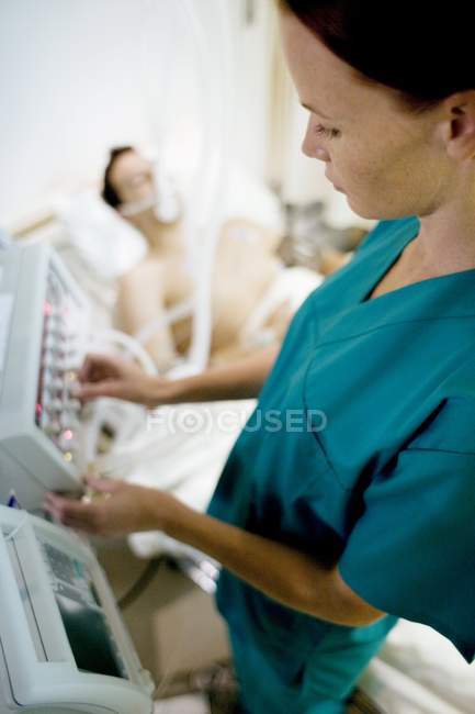 Enfermeira ajustando controles no ventilador ligado ao paciente inconsciente . — Fotografia de Stock