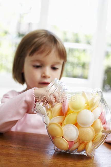 Mädchen nimmt Süßigkeiten aus Glas. — Stockfoto