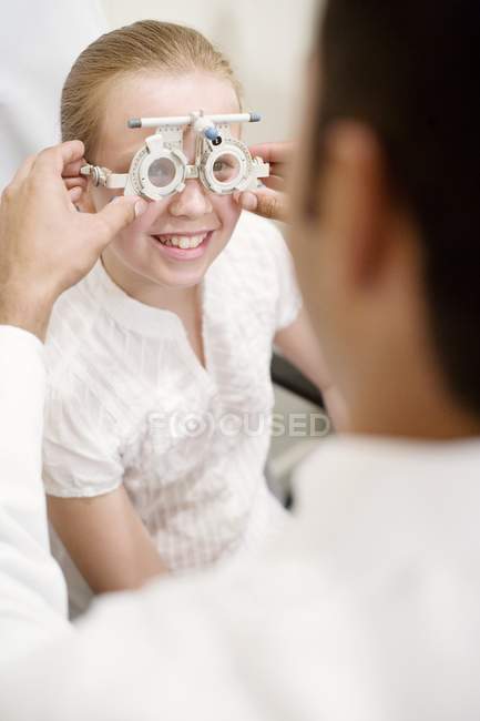 Optician ajustando quadro experimental para exame ocular menina pré-adolescente . — Fotografia de Stock