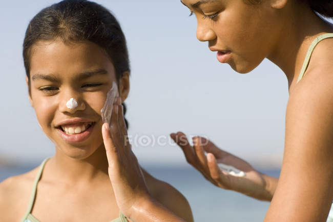 Menina aplicando protetor solar ao rosto irmã . — Fotografia de Stock
