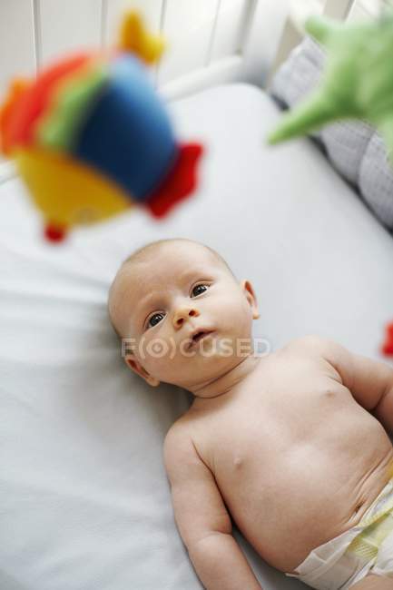 Infant baby boy lying in cot and looking up at toys. — Stock Photo
