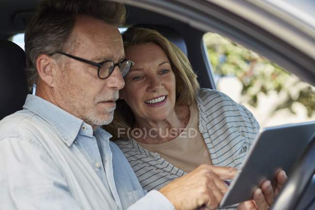 Senior couple sitting in car with digital tablet. — Stock Photo
