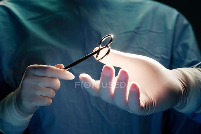 Обрезанный вид ассистента, передающего щипцы хирургу во время операции . — стоковое фото