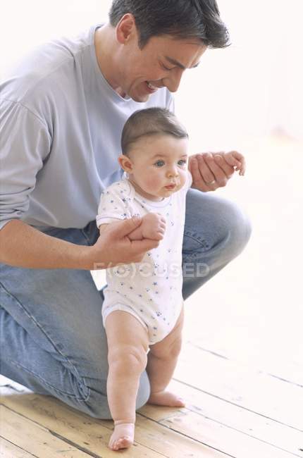 Niño bebé siendo apoyado por el padre en el suelo . - foto de stock