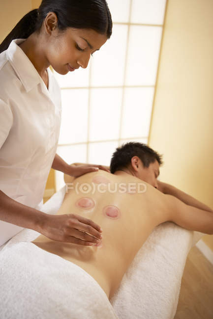 Therapeut entfernt erhitzte Tassen während Schröpftherapie vom Rücken des Klienten. — Stockfoto