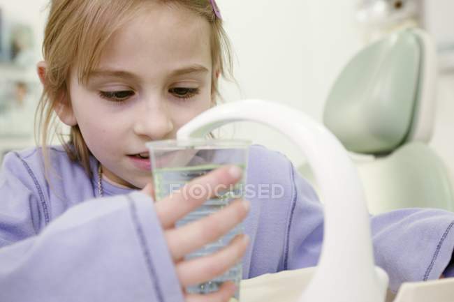 Chica en la sala de tratamiento dental de llenado de vidrio con enjuague bucal antimicrobiano . - foto de stock