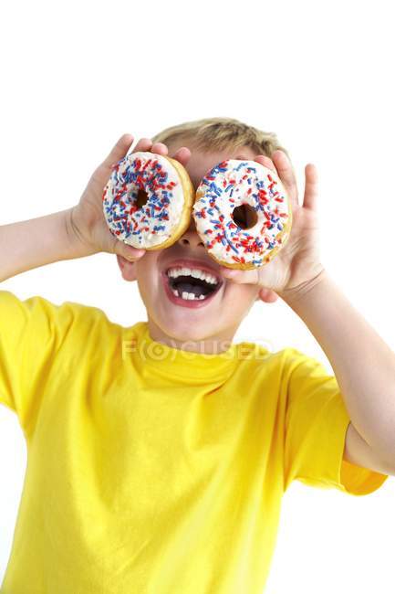 Boy playing and covering eyes with doughnuts. — Stock Photo