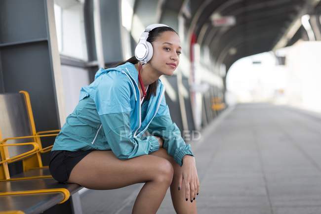 Mulher sentada na plataforma ferroviária usando fones de ouvido — Fotografia de Stock