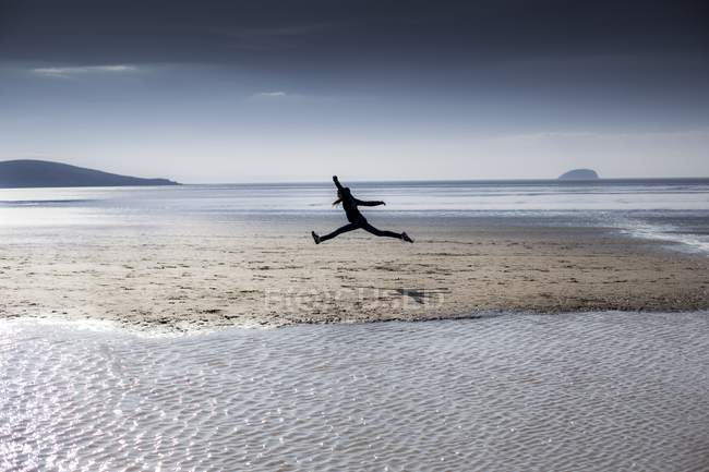 Силуэт человека, прыгающего по пляжу . — стоковое фото