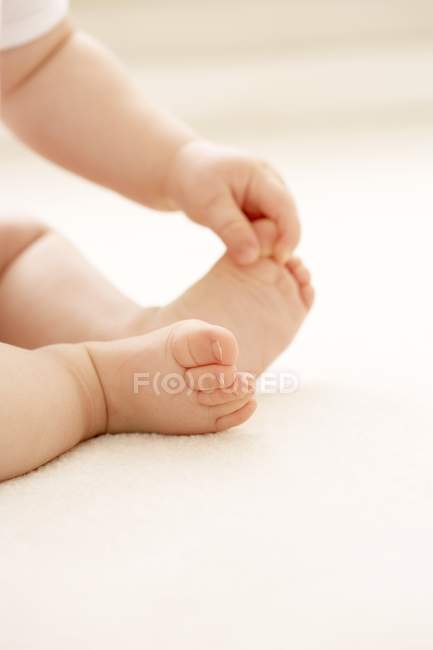 Baby grasping big toe while sitting on floor. — Stock Photo