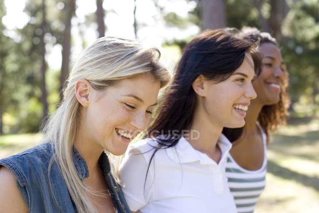 Three young female friends walking and smiling in park. — Stock Photo