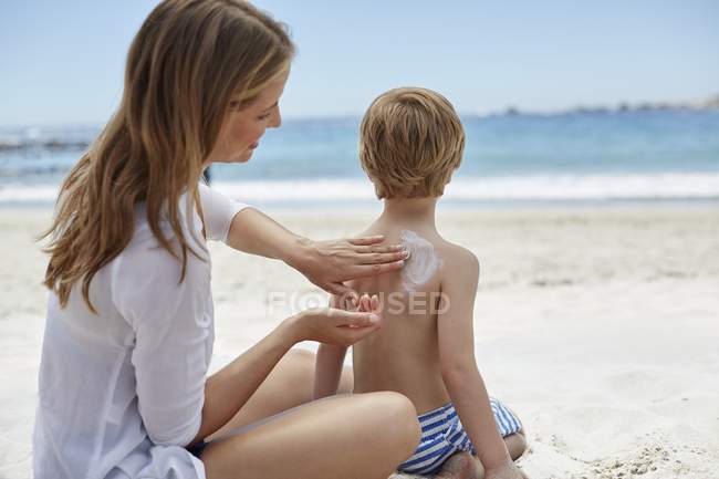 Mère appliquant de la crème solaire à son fils sur la plage
. — Photo de stock